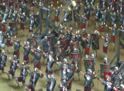 Roman soldiers in silver armor and red tunics march with torches and spears.