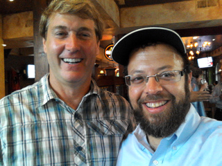 Two men smiling side by side in a restaurant setting.