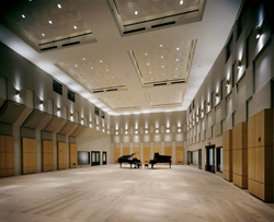 A spacious, modern concert hall with light wood floors, paneled walls, and two grand pianos in the center.