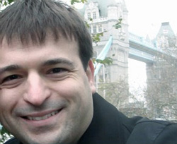 A smiling man in a black jacket with Tower Bridge in the background.
