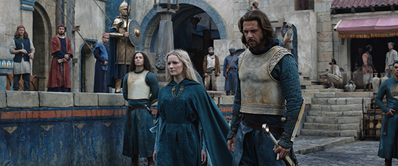 People in historical fantasy costumes stand in a stone village courtyard.