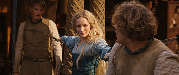 A blonde woman in a blue dress holds a dagger, facing a man in a rustic setting.