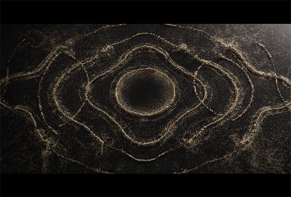 Concentric, wavy patterns formed by fine sand on a dark, textured background.