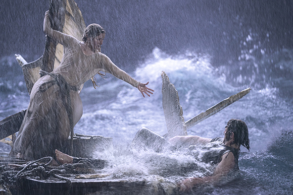 A woman in a light dress reaches toward a man amidst crashing waves and heavy rain.