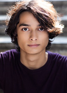 Close-up portrait of a young man with dark wavy hair wearing a dark purple shirt.