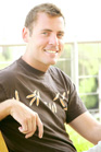 A smiling man wearing a black t-shirt with a light-colored pattern.
