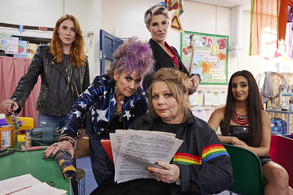 Four women of various ages pose together in a brightly lit classroom.