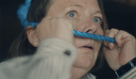 A woman with wide eyes holds a thick blue rope horizontally across her nose and mouth.
