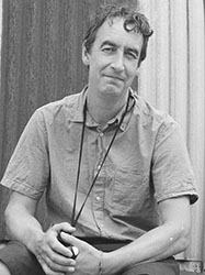 A man with wavy hair wearing a button-down shirt and a lanyard around his neck.