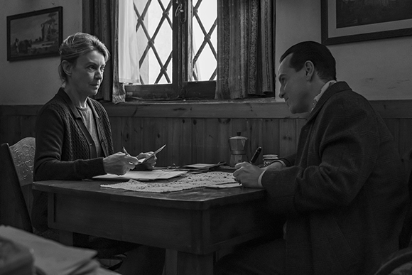 Black and white shot of a man and woman sitting at a table in a room with a lattice window.