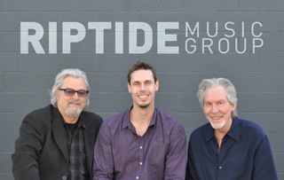 Three men smiling in front of a gray wall with the text Riptide Music Group.
