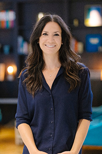 A woman with long dark hair smiling while wearing a dark blue button-down shirt.