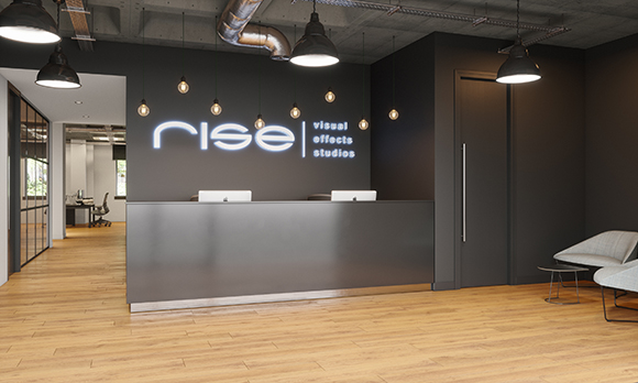 A modern dark reception desk with a glowing Rise Visual Effects Studios sign on a black wall.