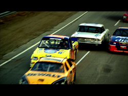 Several colorful stock cars racing closely together on an asphalt track.