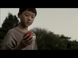 A young boy looks down while holding a small red and white ball outdoors.