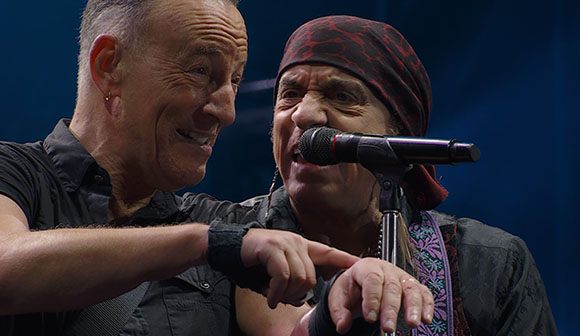 Two men smiling closely together on a stage with a microphone in the foreground.