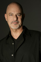A bald man with a goatee wearing a black button-down shirt over a black v-neck shirt.