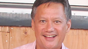 A smiling man with short brown hair wearing a light pink collared shirt.