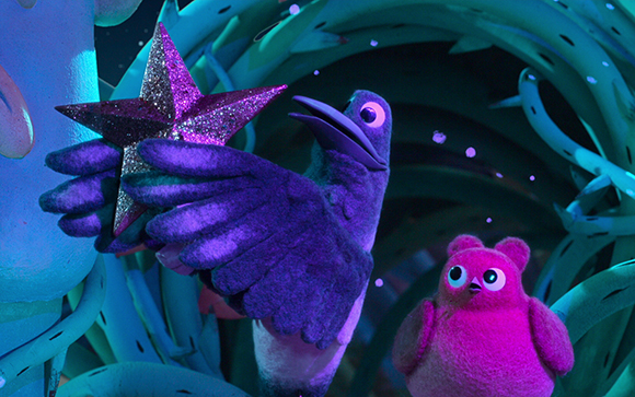 A purple felt bird holds a large pink glittery star near a small pink fuzzy creature in a blue forest.