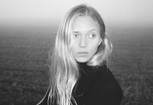 Black and white portrait of a blonde woman with long hair looking off-camera against a blurred landscape.