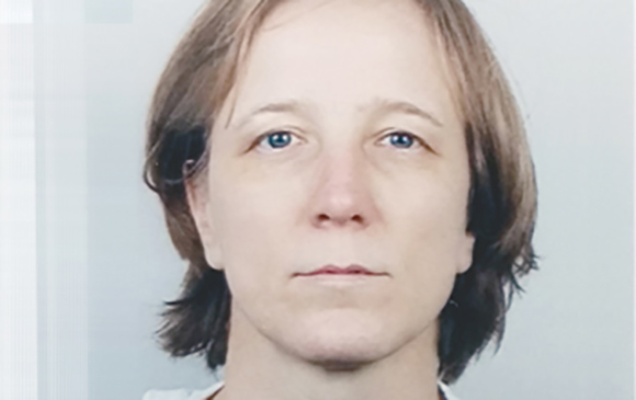 A close-up portrait of a woman with light brown hair and blue eyes looking directly at the camera.