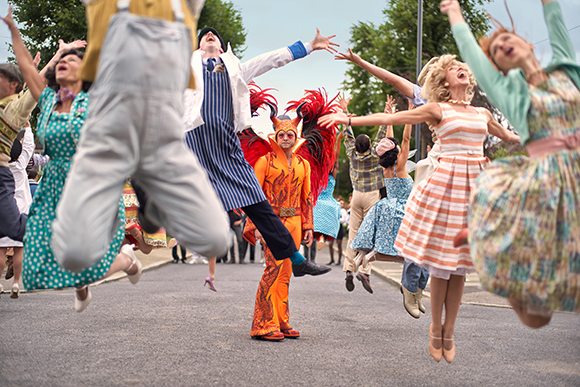 A group of people in colorful vintage clothing jumping and dancing joyfully in a street.