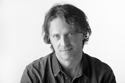 Black and white headshot of a man with wavy hair looking toward the camera.