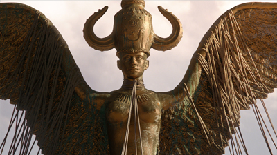 A golden statue of a winged figure wearing a tall, horned headdress against a cloudy sky.