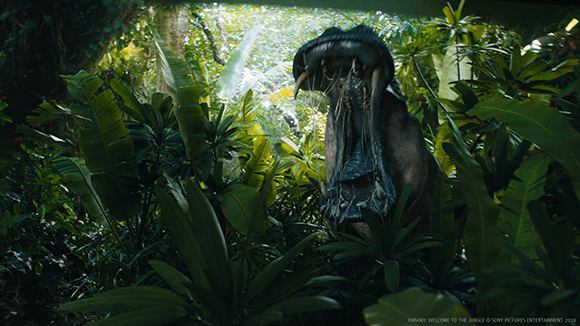 A large dinosaur with an open mouth emerges from thick green tropical leaves.