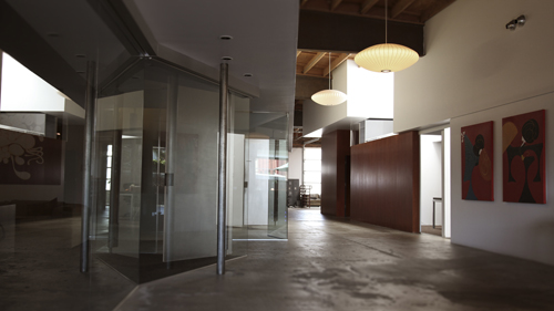 A modern open-plan interior featuring glass walls, polished concrete floors, and large hanging pendant lights.