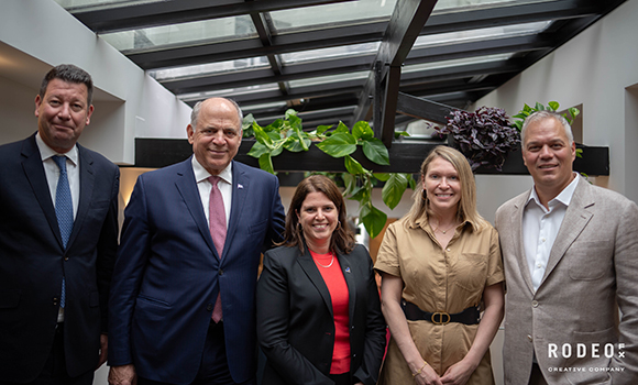 Five people in professional attire standing together under a glass skylight ceiling.