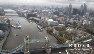 Aerial view of the River Thames, Tower Bridge, and the London skyline under a cloudy sky.