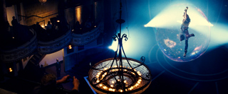 A performer floats inside a glowing, illuminated sphere above a dark theater audience.