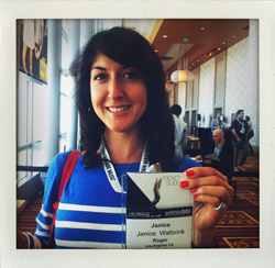 A woman with dark hair and a blue and white striped sweater smiles and holds up a conference badge that reads Janice Waltbrin