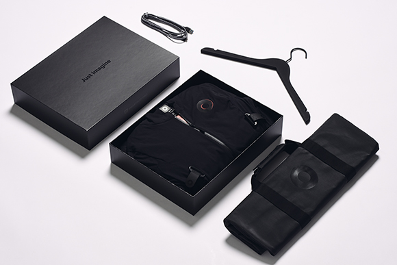 An open black box with a black garment, a black hanger, a black folded bag, and a charging cable on a white surface.
