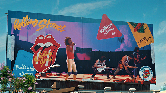 A large billboard displaying The Rolling Stones logo, band members performing, and various graphic elements.