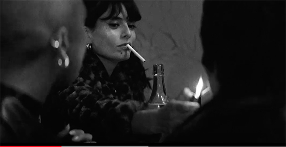 Black and white close-up of a woman with a cigarette in her mouth in a dark room.