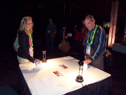 A woman and a man stand at a table with interactive elements, possibly at a conference or event.