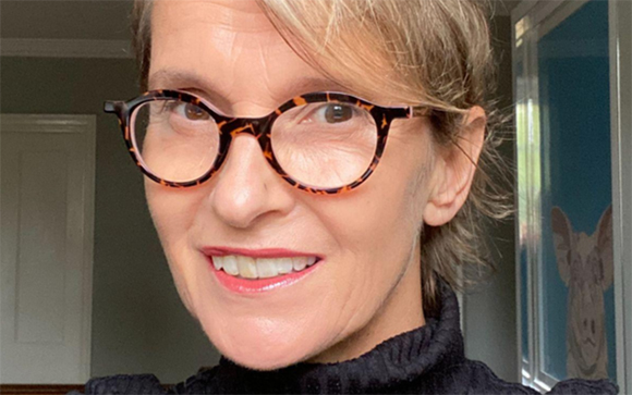 A woman with short blonde hair and tortoiseshell glasses smiling at the camera.
