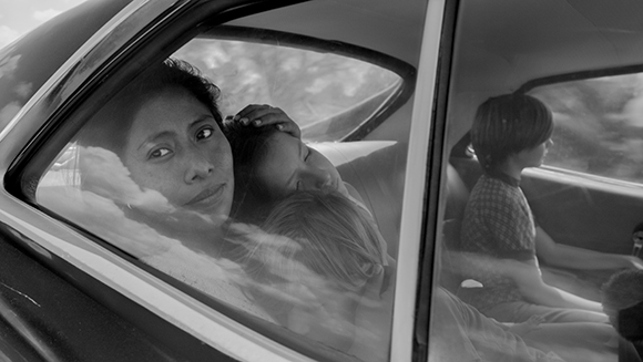 Black and white reflection in a car window showing a woman and a child leaning against each other.