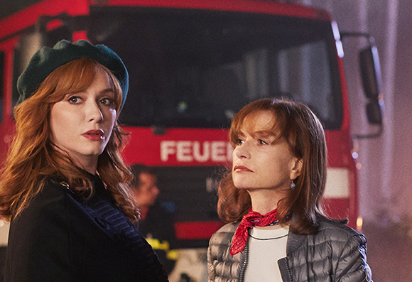 Two women with reddish hair look off-camera in front of a red fire truck.