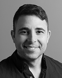 A black and white headshot of a man with short dark hair smiling at the camera.