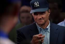 A man wearing a navy blue New York Yankees cap and suit jacket points his finger toward the viewer.