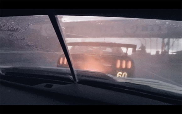 View through a windshield of a car with glowing taillights driving through thick fog or dust.
