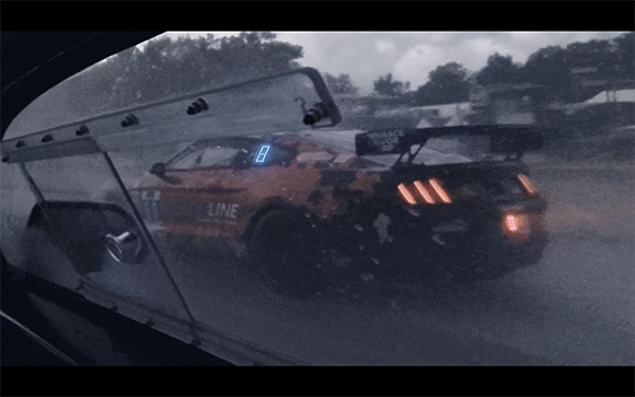 A race car with number 8 on its window drives through heavy rain on a dark track.