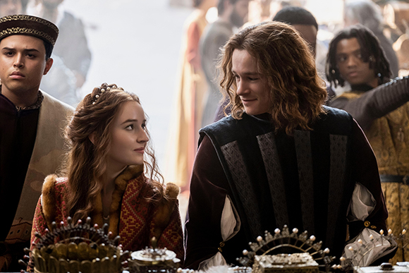 A young woman with braided hair looks up at a smiling man with wavy hair in historical costumes.