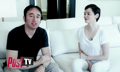 A man in a black shirt and a woman in a white shirt sit on a white couch.