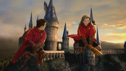 Two people wearing red capes and boots flying through the air in front of a large castle at sunset.