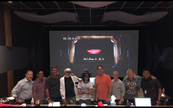 A group of nine people standing in a row in a dark room in front of a large projection screen.