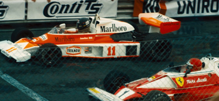 Two vintage white and orange Marlboro-sponsored racing cars on a track.